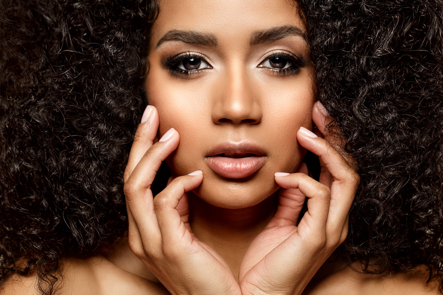woman of color with beautiful hair skin and nails touching her face.